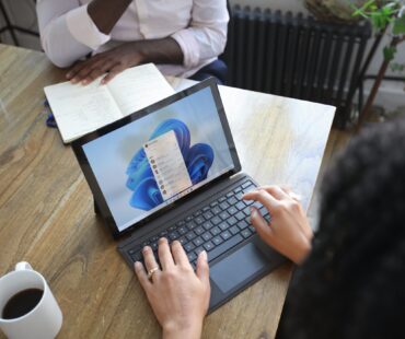 Overhead view of two people at a table working with a Microsoft laptop and notebook