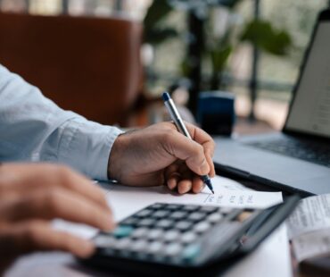 Free A person calculating finances with a calculator and pen on a desk indoors. Stock Photo
