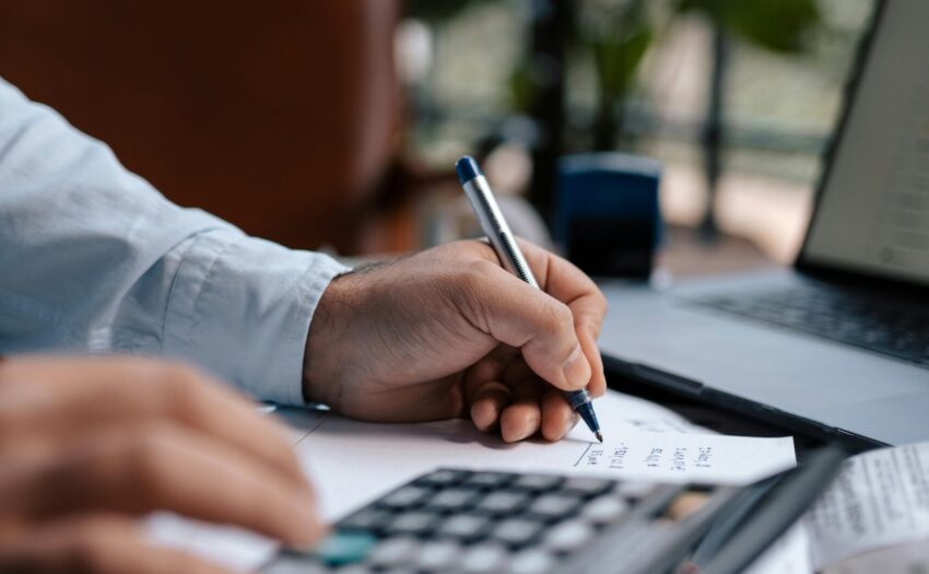 Free A person calculating finances with a calculator and pen on a desk indoors. Stock Photo