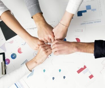 Free Colleagues celebrate success with a fist bump over financial charts depicting teamwork and unity. Stock Photo